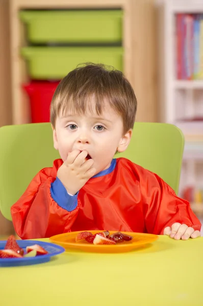 Young boy eating fruit in a nursery room — Stock Photo, Image