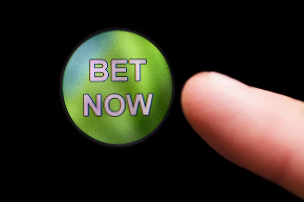 Палец нажимает кнопку "Bet Now" на черном сенсорном экране — стоковое фото