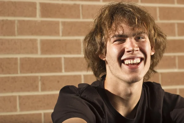 Joven sentado sonriendo frente a una pared de ladrillo — Foto de Stock