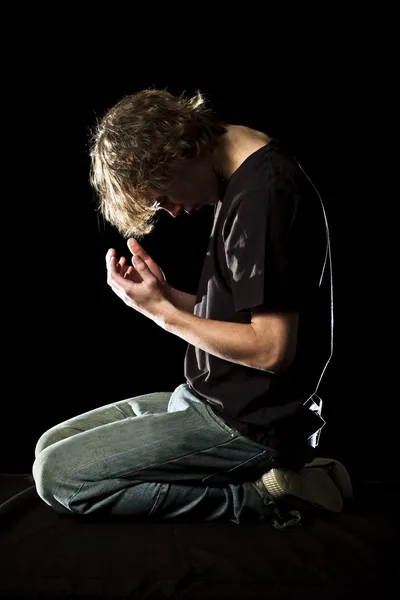 Mladý muž klečí a modlí se — Stock fotografie