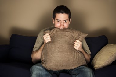 Man bites pillow in fear while watching TV clipart