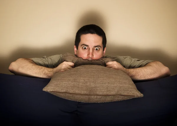 Frightened man hides behind couch watching TV — Stock Photo, Image