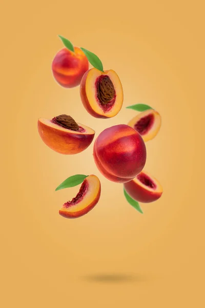 Flying fresh ripe nectarines - peaches with green leaves levitating  against yellow background. Creative minimal concept of food levitation.