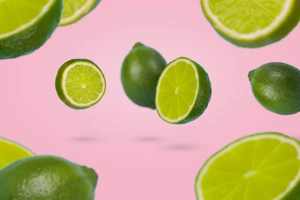 Floating levitating fresh lime on pastel pink background. Vitamins, healthy diet concept. Minimal fruit idea. Whole and Sliced lime floating in the air. Creative concept with flying fruits.
