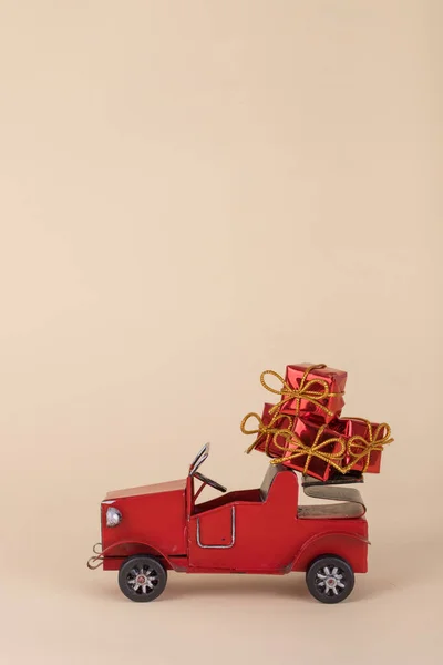 Creative idea with old red car carrying Christmas or New Year  gifts isolated on a beige background. Minimal  Holiday concept.