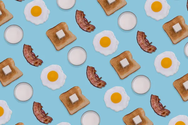 图案由煎蛋 脆咸肉片 烤面包和牛奶杯在淡蓝色背景 最小和创造性的早餐概念 顶部视图 平躺在床上 — 图库照片