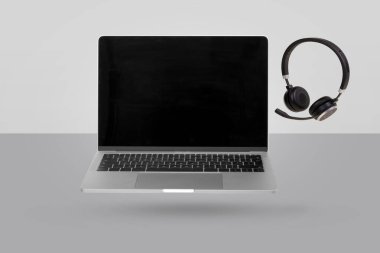 Boş ekranlı dizüstü bilgisayar ve gri arka planda havaya yükselen kulaklık. Yaratıcı asgari altyapı. Pop sanat, kavramsal sanat. Reklam, pazarlama ve reklamlar için uygun.