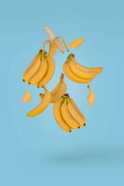 许多新鲜的香蕉在空气中飘扬 背景是蓝色的 最低水果概念 — 图库照片
