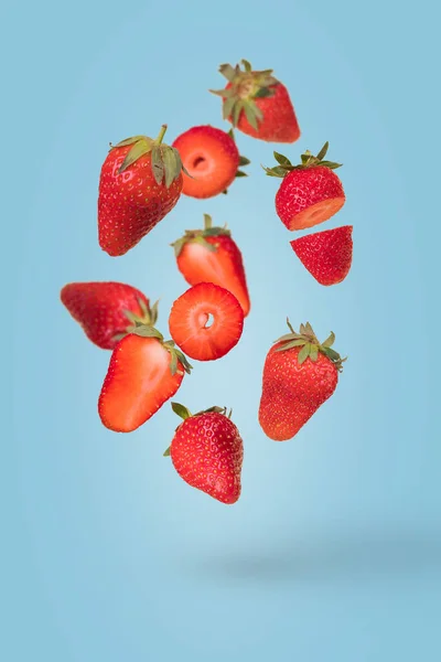 有创意的构图 漂浮着成熟的草莓 蓝色背景 维生素 新鲜健康食品的概念 最小的水果的想法 切碎的草莓和整个草莓在空气中飘扬 免版税图库照片
