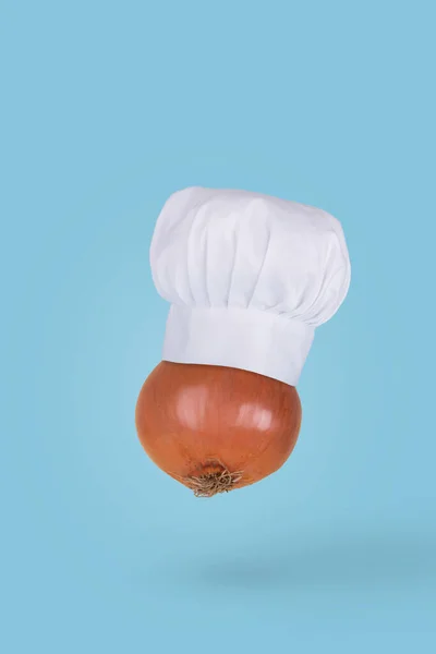 新鲜的洋葱 头戴厨师帽 空气中飘扬 背景是蓝色的 健康食品配料概念 最低限度食物概念 — 图库照片