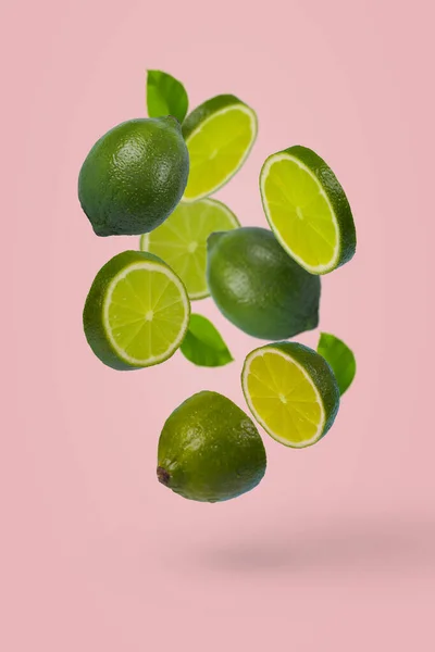 パステルピンクの背景に隔離された空気中を飛んで全体とスライス石灰と創造的なアイデア 最小限の果物の概念 ビタミン 健康的な食事の概念 — ストック写真
