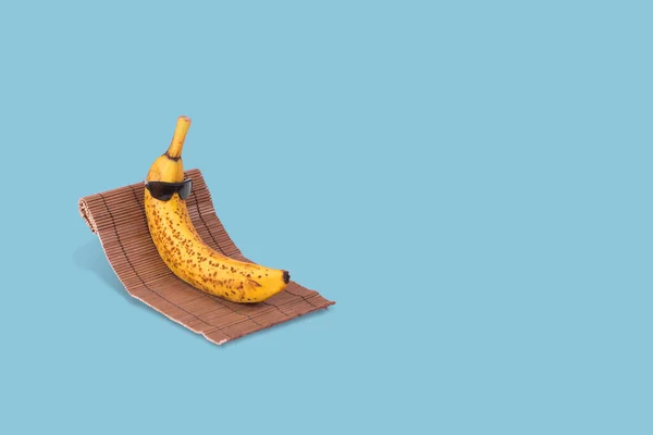 创意有趣的想法 太阳镜上的香蕉躺在蓝色背景的太阳床上 简约的旅游理念 夏日时尚的热带水果 夏天的色彩心情 时尚与潮流 — 图库照片