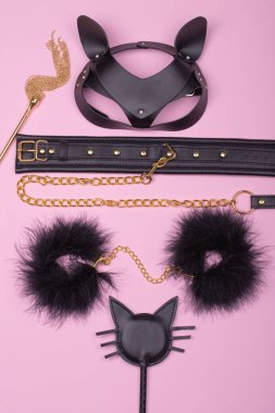 BDSM için erotik oyuncaklar. Kırbaç, kelepçe, deri tasma ve açık pembe arka planda maskeyle yapılan cinsel kölelik oyunu. Özel seks oyunları. 