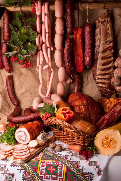 Wurst, Schweinefleisch, Salami und Gemüse im Hintergrund. Stillleben mit Fleisch Stockbild