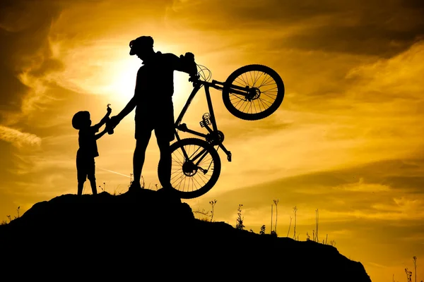 Montanha silhueta motociclista com seu filho no topo da colina . — Fotografia de Stock