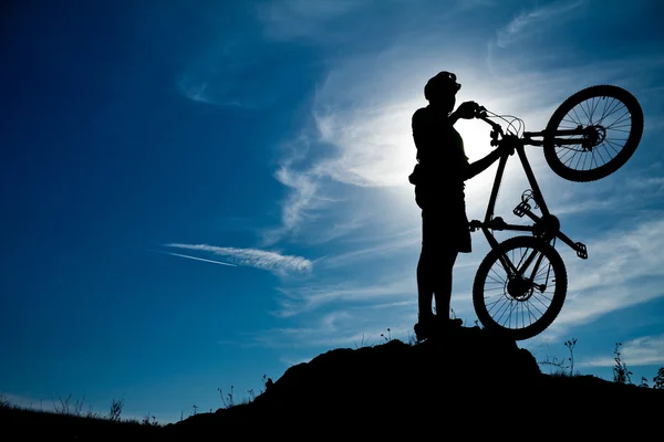 Горный велосипедист с велосипедом над драматическим небом — стоковое фото
