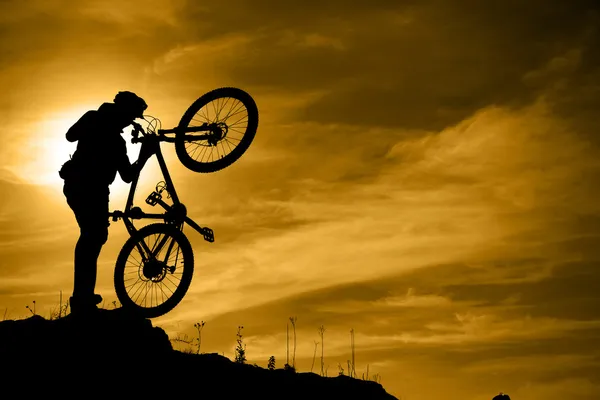 Mountainbiker mit Fahrrad über dramatischen Himmel lizenzfreie Stockfotos