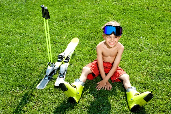 Ritratto di attraente bambino seduto sull'erba con sci — Foto Stock
