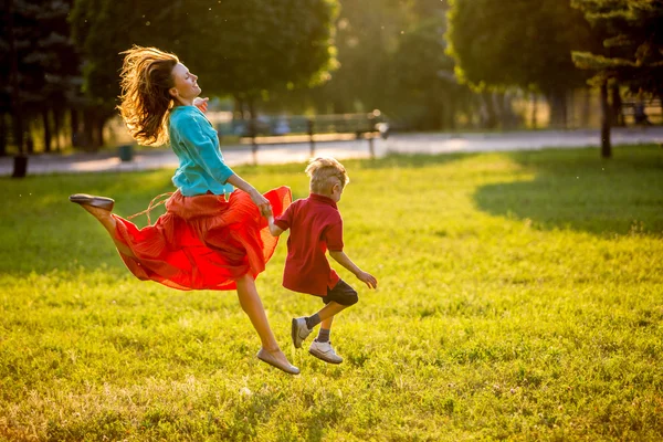 Madre spensierata e bambino si divertono nel parco estivo, corrono e saltano in movimento. retroilluminato — Foto Stock