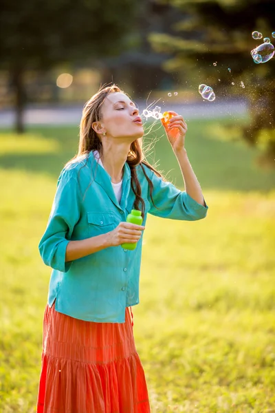 Gelukkige vrouw portret blazen van zeepbellen in het park — Stockfoto