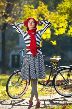 genç bir kadın sonbahar Park, elleri başının arkasında duran ve gökyüzüne bakarken eğleniyor. Retro şehir bisikleti arkasında.