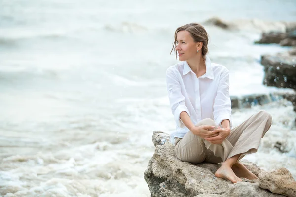 Мечтающая молодая женщина сидит у моря — стоковое фото