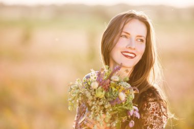 Günbatımında bir alanda gülümseyen güzel kadın