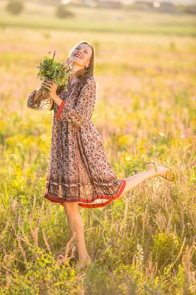 Mulher sorridente bonita em um campo no por do sol — Fotografia de Stock