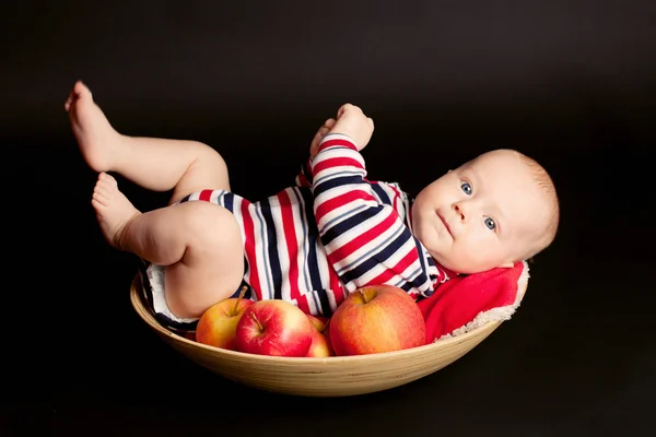 Liten pojke med röda äpplen på en svart bakgrund — Stockfoto