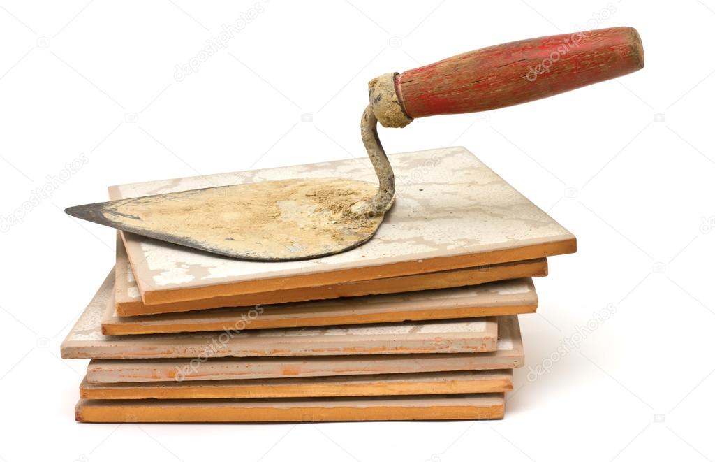 Old dirty construction trowel on pile of tiles isolated on white