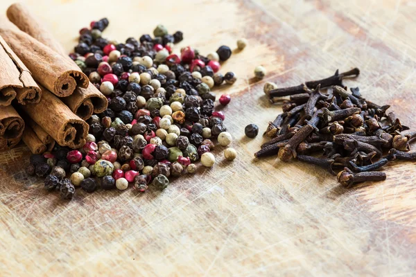 Mixed pepper, cinnamon, cloves on wooden background — Stock Photo, Image