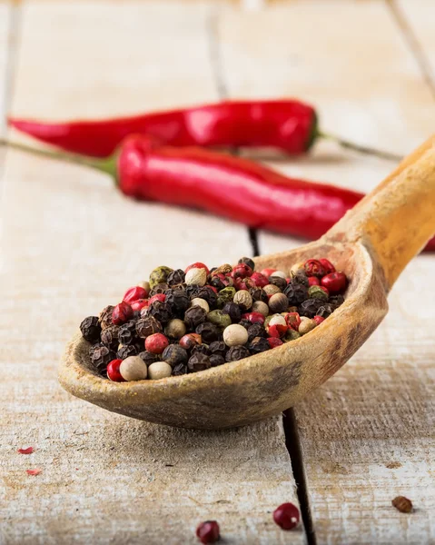 Mixed pepper in old spoon on wooden background — Stock Photo, Image