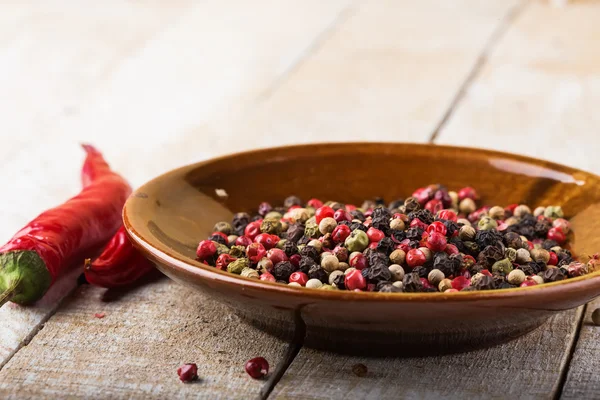 Mixed pepper on plate on wooden background — Stock Photo, Image