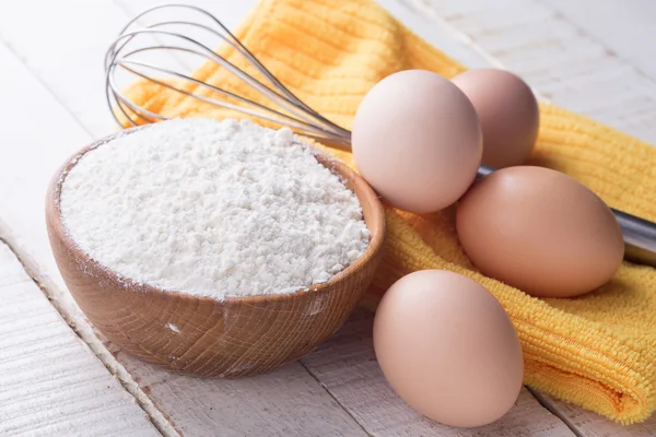 Mehl in Holzschüssel, Eier auf dem Tisch. — Stockfoto