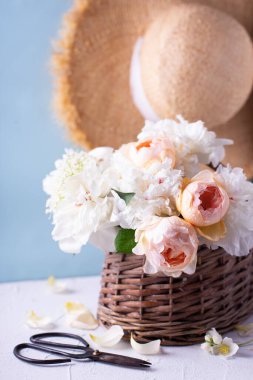 İçinde romantik yaz gülleri ve şakayık çiçekleri olan bir kartpostal sepette ve mavi arka planda şapka. Seçici odaklanma. Durgun hayat.  