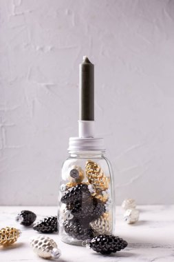 Noel süslemeleriyle dolu bir arka plan. Altın, siyah, gümüş renkli dekoratif koniler ve gri desenli arka planı olan cam şamdan. İskandinav minimalist tarzı. Durgun hayat.