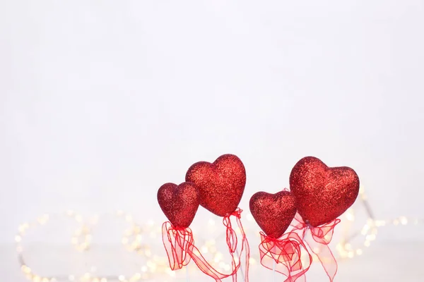 St. Valentine Day background. Border from colorful  red hearts and fairy lights  against white textured background. Selective focus. Place for text.