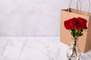 Kırmızı renkli yaz gülleri çiçekleri ve gri desenli arka planda mevcut kağıt torba. Seçici odaklanma. Durgun hayat. Metin için yer.