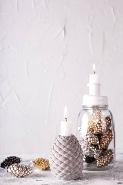 Noel süslemeleriyle dolu bir arka plan. Beyaz yanan mumlar, altın sarısı, siyah, gümüş renkli dekoratif koniler gri desenli şamdanlar. İskandinav minimalist tarzı. Durgun hayat.