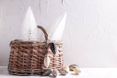 Noel kompozisyonu. Dekoratif beyaz tatil ağaçları ve gri desenli arka planda siyah ve gümüş süslemeleri olan kırsal bir sepet. İskandinav minimalist tarzı. Durgun hayat. Boşluğu kopyala.