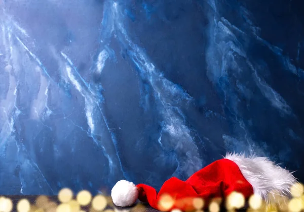 新年やクリスマスの装飾の背景 深い青色のマルムール壁に対するサンタクロースの赤い帽子 ホリデーボケライト まだ生きてる クリスマスのコンセプト テキスト用の場所 冬休みはがき — ストック写真