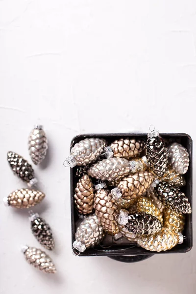 Christmas decorations. Metallic box with glass gold, black, silver decorative cones on white  textured background. Scandinavian minimalistic style. Still life. Place for text.