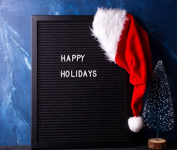 背景与新年或圣诞装饰 黑色的木板 红色的圣诞老人帽 蓝色的树靠着深蓝色的土墙 安静的生活 圣诞节的概念冬季假期明信片 — 图库照片