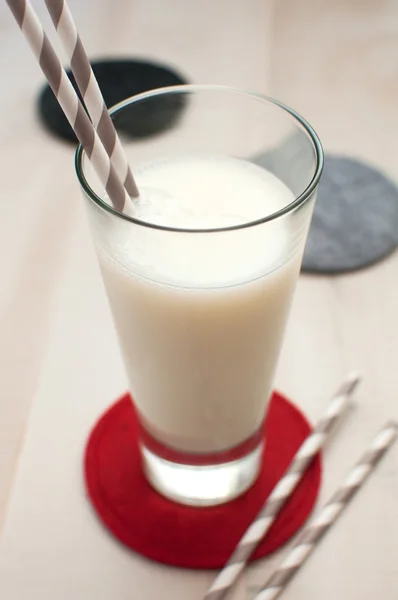 Glass of milk with striped straws and coaster — Stock Photo, Image