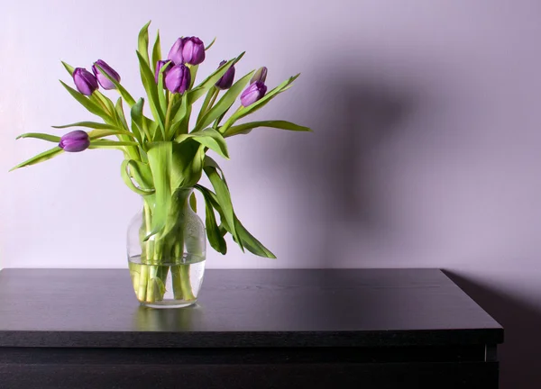 Jarrón con tulipanes morados sobre mesa negra Imagen De Stock