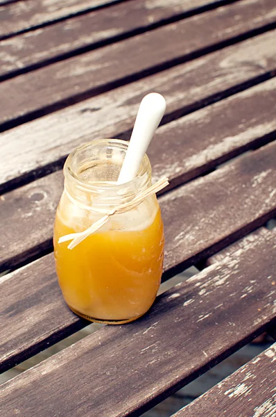 Glas mit Honig und Löffel auf dem Tisch draußen — Stockfoto