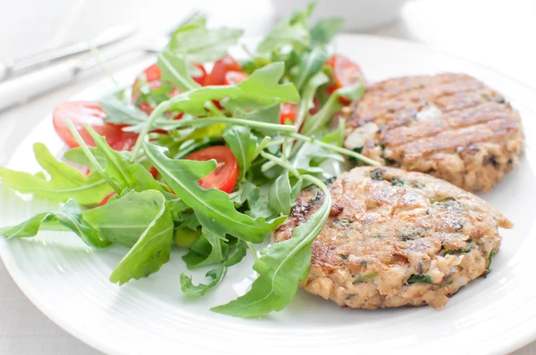 Ground fish patty with arugula tomato salad — Stock Photo, Image