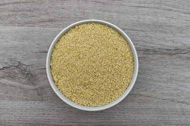 Tahta arka planda izole edilmiş bir kase ham kuskus. Üst görünüm.