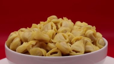 Ham Tortellini kırmızı arka planda dönüyor. Geleneksel İtalyan makarnası