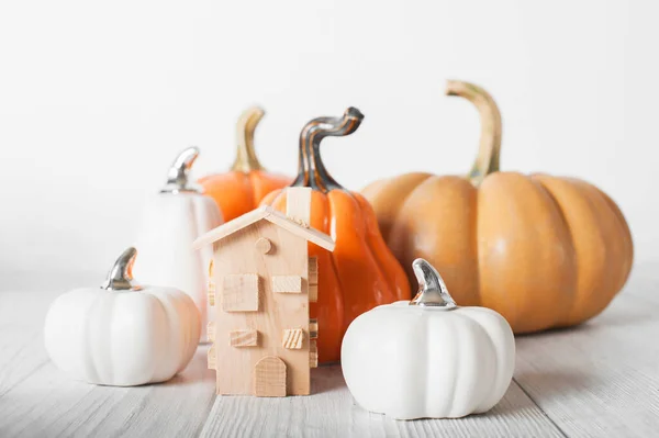 Autumn house insurance, sale, rent concept. White decorative pumpkins and autumn yellow leaves with miniature wooden house close-up and copy space.